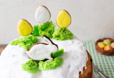 Paskalya pastası, beyaz kremayla süslenmiş kuru üzüm ve Paskalya yumurtası şeklinde zencefilli ekmek ve yeşil kareli masa örtüsü üzerinde yeşil çimenler üzerinde bir tavşan. Kırsal