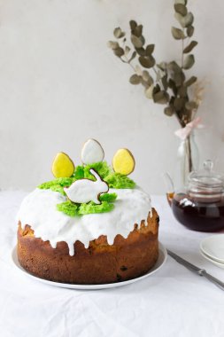 Paskalya pastası, beyaz kremayla süslenmiş kuru üzüm ve Paskalya yumurtası şeklinde zencefilli ekmek ve beyaz masa örtüsü üzerinde yeşil çimenler üzerinde bir tavşan. Aile yemeği için şenlikli hamur işleri. Boşluğu kopyala.