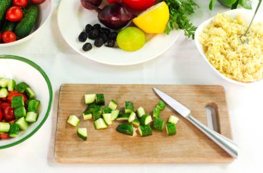 Tahta kesme tahtasında dilimlenmiş salatalık dilimleri. Masadaki malzemelerle birlikte Orzo salatası hazırlama süreci. Vejetaryen yemeği kavramı. Yatay yönelim.