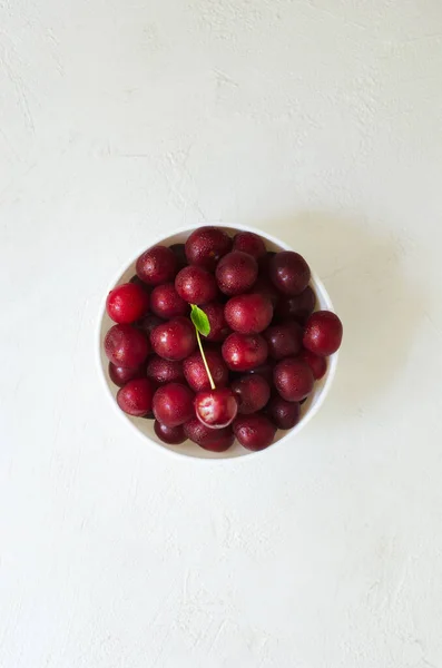 Many ripe red cherries in a white ceramic bowl on a light background. The concept healthy food. Vertical orientation. Top view. copy space.
