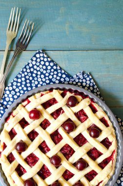 Mavi ahşap bir masada yuvarlak şekilli ev yapımı vişneli turta. Geleneksel pişirme kavramı. Mevsimlik turta. Dikey yönelim. Üst görünüm. Boşluğu kopyala.