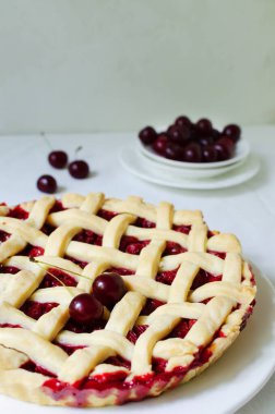 Masanın üzerinde beyaz bir masa örtüsü olan büyük beyaz bir tabakta ev yapımı vişneli turta. Geleneksel pişirme kavramı. Mevsimlik turta. Dikey yönelim.