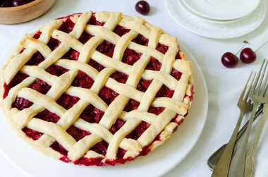 Homemade cherry pie on a large white plate with ribs on a white tablecloth on the table. The concept of traditional baking. Seasonal pie. Horizontal orientation.
