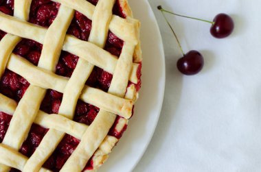 Homemade cherry pie on a large white plate on a white tablecloth on the table. The concept of traditional baking. Seasonal pie. Horizontal orientation. Top view. Copy space