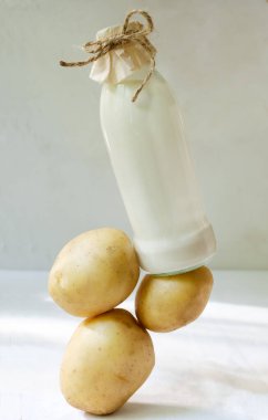 Masanın üzerinde patates sütü olan cam şişe. Sağlıklı beslenmede yeni bir eğilim. Yiyecek uçurma konsepti. Vejetaryenler için sebze sütü. Dikey yönelim.