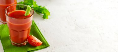 Şeffaf cam bardakta domates suyu ve beyaz arka planda yeşil bir peçetede kereviz sapı. Vejetaryen yemeği kavramı. Yatay oryantasyon. Seçici odaklanma. kopyalama alanı. Pankart