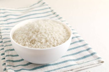 Dry camollino rice in a white ceramic bowl on a striped kitchen towel. The concept of vegan food. Healthy Eating. Copy space. Selective focus. Horizontal orientation.