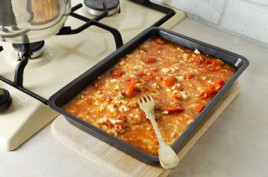 The process of making feta pasta. Baked cheese and tomatoes with herbs, olive oil in a baking dish and spaghetti in a shiny pot. Horizontal orientation. Selective focus