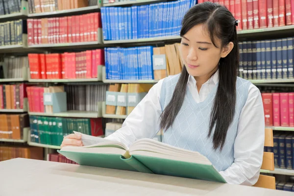 Estudiante asiático leyendo libro en biblioteca en la universidad — Foto de Stock