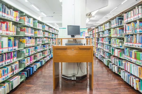 Datorn i ett bibliotek med många böcker och hyllor i backgro — Stockfoto