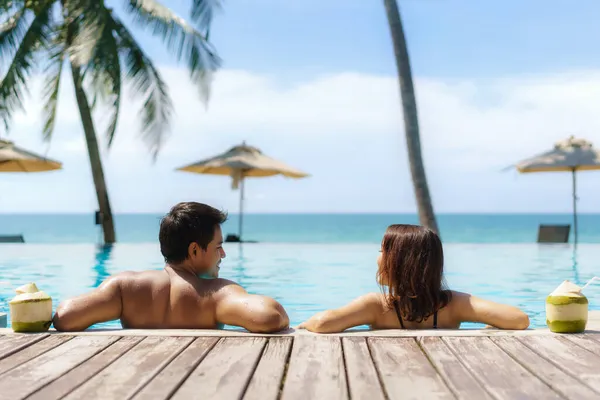 夏の旅行休暇のコンセプト ココナッツと旅行者のアジアのカップルは 海のビーチとヤシの木の背景を持つ高級インフィニティプールホテルリゾートでリラックス — ストック写真