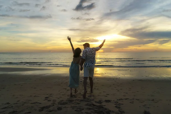旅行休暇中にビーチで美しい夕日を楽しむロマンチックなアジアのカップル立って手を握っている — ストック写真