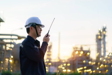 Asian man technician Industrial engineer using walkie-talkie and holding bluprint working in oil refinery for building site survey in civil engineering project.