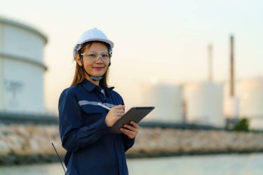 Asian engineer woman are checking the maintenance of the oil refinery factory at evening via digital tablets