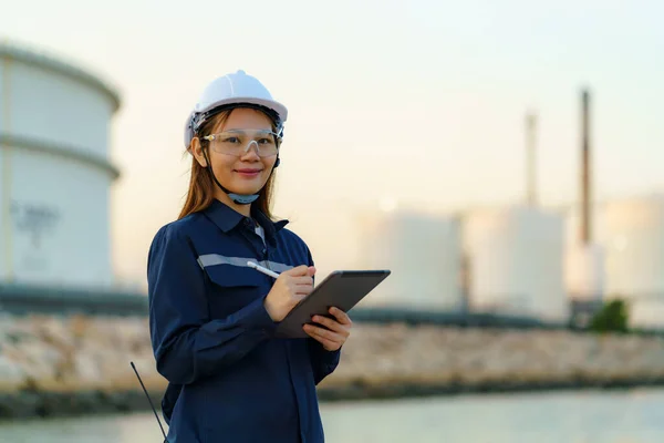 アジアのエンジニアの女性は デジタルタブレットを介して夕方に石油精製工場のメンテナンスをチェックしています — ストック写真