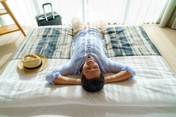 スーツケースを着たアジア人男性は 夏休みの旅行中に到着した後 リゾートの彼の部屋にベッドの上に横たわっていました — ストック写真