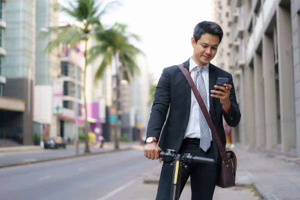 亚洲商人正在驾驶电动车 并利用他的手机打开了一张地图 以申请在早上检查城市的公路路线 — 图库照片