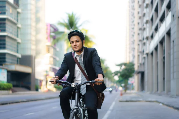 スーツ姿のアジア人ビジネスマンが通勤のために街中の自転車に乗っている エコ交通概念 — ストック写真