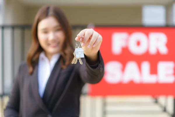 アジアの不動産業者や不動産業者の女性笑顔と家の前で家の鍵を示すと赤いファイルを保持 — ストック写真