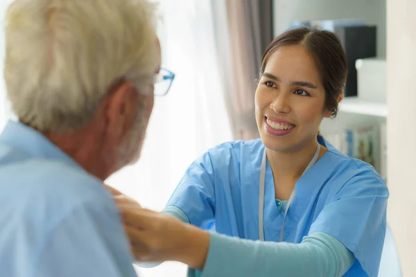 Young Asian woman nurse helping get dress to disabled elderly man in bed at retirement home. Millennial caregiver assisting handicapped senior patient, taking care of older male indoors