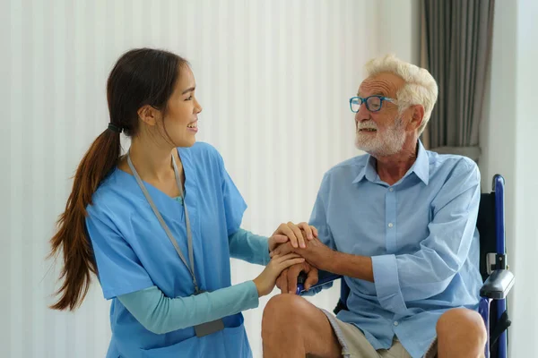 Asian nurse sitting on a hospital bed next to an older man helping hands, care. Elderly patient care and health lifestyle, medical concept.