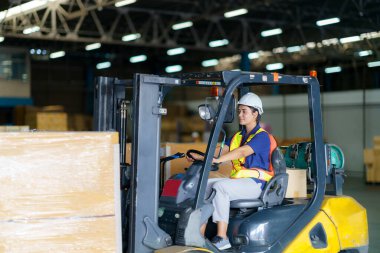 Asian beautiful woman driver drive fork lift car in industry with smile, ability of girl and diversity of career wearing helmet in reflective vest working on vehicle