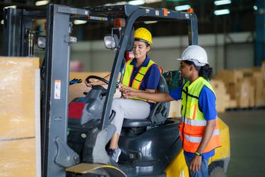 Asian man teaching woman driver drive fork lift car in industry with smile, ability of girl and diversity of career wearing helmet in reflective vest working on vehicle