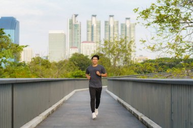 Asyalı sağlıklı sporcu sabah koşuyor. Şehir parkında..