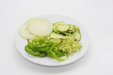 Beyaz arka planda kabak tadı ve dolma biber, soğan ve kabak dilimleri var.