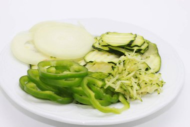 Beyaz arka planda kabak tadı ve dolma biber, soğan ve kabak dilimleri var.