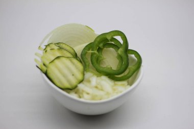 Beyaz arka planda izole edilmiş bir kasede doğranmış soğan ve kabak dilimleri ve dolma biber.