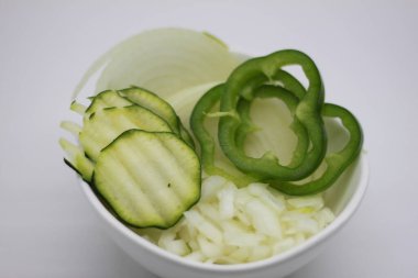 Beyaz arka planda izole edilmiş bir kasede doğranmış soğan ve kabak dilimleri ve dolma biber.