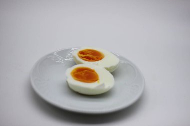 Haşlanmış yumurta yarı yarıya soyulup, beyaz arka planda izole edilmiş bir tabakta açılır.