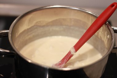 Kırmızı kaşıkla metal bir tencerede ev yapımı sütlaç pişirmek.