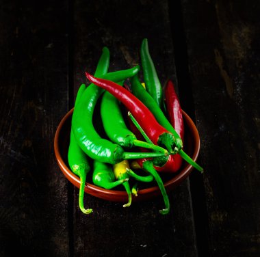 Red And Green Hot Chili Peppers in bowl over wooden background clipart