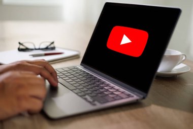 Bangkok, Tayland - 25 Nisan 2022: YouTube sitesinde ekranında YouTube logosu olan bir adam dizüstü bilgisayar kullanıyor. YouTube dünyanın en popüler internet sitesidir.