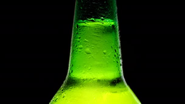 Zamknąć zimną szyję butelki piwa kroplami wody. Zimne światło i orzeźwiające piwo na czarnym tle. Zielona butelka piwa.. — Wideo stockowe