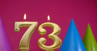 73 numaralı doğum günü pastası mumu yanıyor. Mutlu yıllar yıldönümü kutlaması konsepti. Arka planda doğum günü şapkası