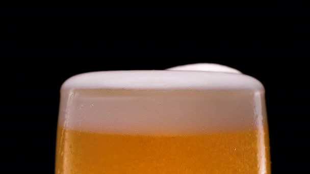 Movimento lento. Lager cerveja derramando com bolhas e espuma no fundo preto — Vídeo de Stock