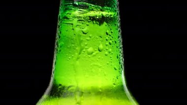 Bira şişesinin soğuk boynunu su damlalarıyla kapatın. Siyah arka planda soğuk ışık ve ferahlatıcı bira. Yeşil bir bira şişesi.