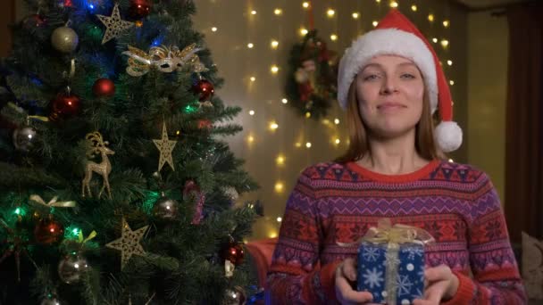 Jong schattig vrolijk gelukkig vrouw in kerst santa hoed geeft u een geschenk doos — Stockvideo
