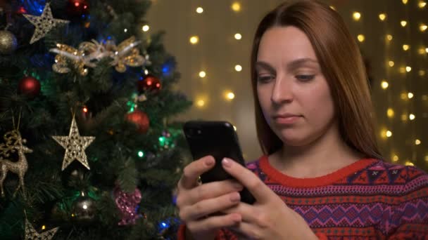 Donna in maglia maglione utilizzando il cellulare che celebra il Natale a casa — Video Stock