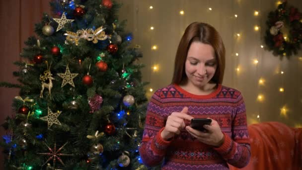 Mujer sosteniendo el teléfono inteligente en las manos y utilizando el móvil. Luces borrosas de Navidad en el fondo. Mujer adulta mensajes de texto SMS, pago, compra — Vídeo de stock