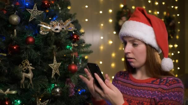 Молодая веселая счастливая женщина в рождественской шляпе Санты с помощью мобильного телефона — стоковое видео
