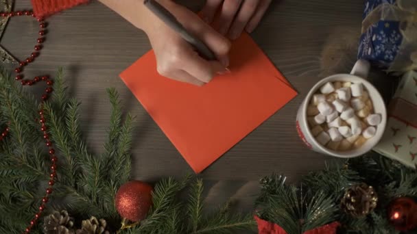 Una donna mano scrivendo un biglietto di Natale con una penna, circondata da decorazioni natalizie — Video Stock