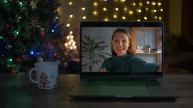 Genç bir kadın el sallıyor ve bir video çağrısında gülümsüyor. Noel zamanı.