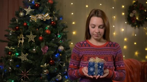Веселая молодая женщина предлагает подарочную коробку на камеру и улыбается. Концепция Рождества — стоковое видео