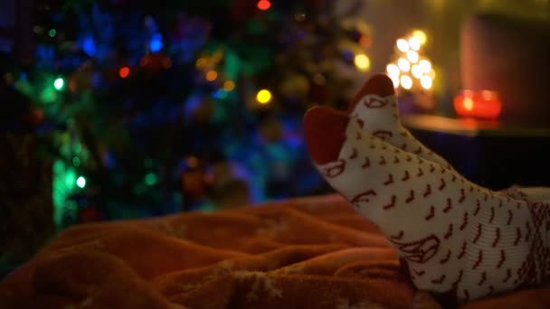Nahaufnahme eines Beinpaares in Weihnachtssocken neben einem Weihnachtsbaum. — Stockvideo