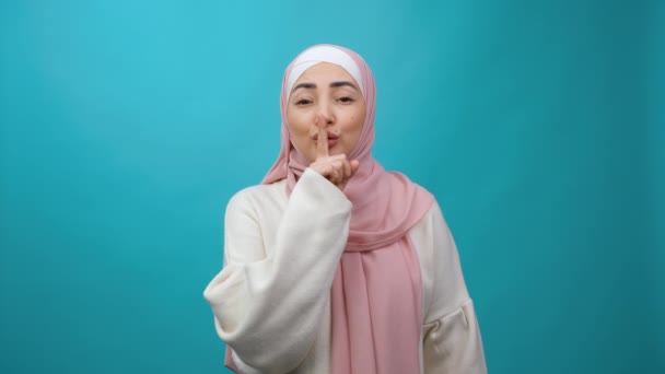 Silencio. Mujer musulmana joven en hiyab silenciando con el dedo en los labios gesto, pidiendo guardar silencio y mirando a la cámara con expresión seria enojado. Cultura y religión islámica tradicional. — Vídeos de Stock