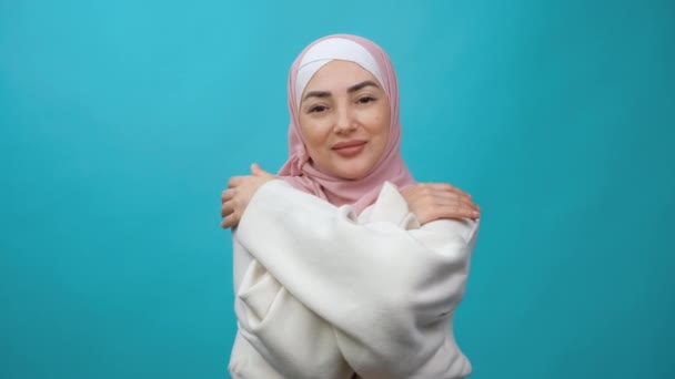 Wanita muslim muda yang baik hati dalam jilbab mengulurkan tangan dengan isyarat isyarat, merangkul dirinya sendiri untuk menunjukkan betapa dia mencintai Anda dan ingin memeluk. dalam ruangan terisolasi — Stok Video